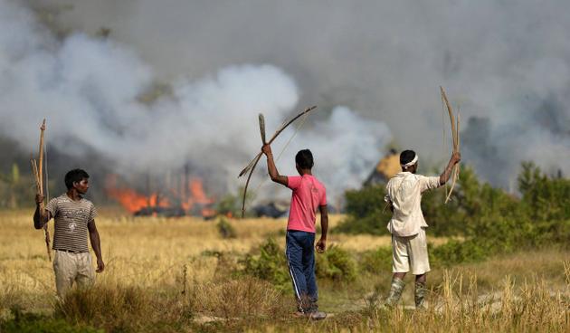 Adivasi men stand guard to gutted houses of Bodos